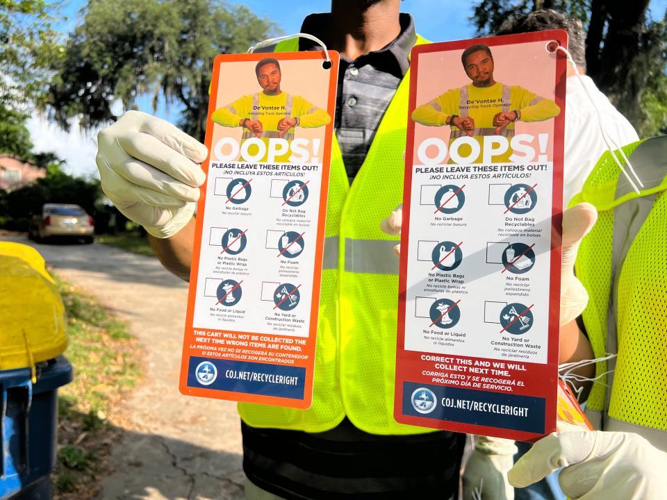 Recycling bin inspectors Fredrick David (left) and Elisah McDonald (right) show the two "oops tags" that could be attached to Jacksonville residents' recycling bins during a media walk-through May 12, 2023. The orange tag is given as a warning. The red tag means the bin was rejected and will not be picked up until the trash is removed.