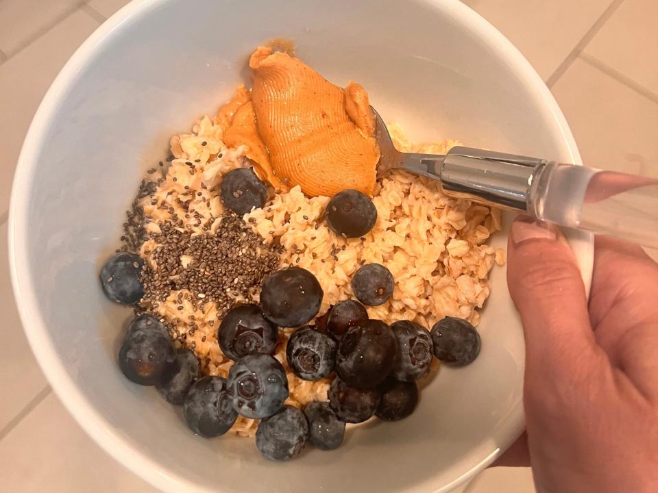 hand holding a bowl of oatmeal with peanut butter chia seeds and blueberries