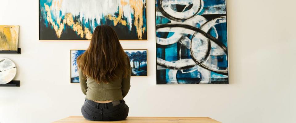 Young female visitor looking reflective while sitting on a bench and admiring the various paintings on the wall of an art gallery