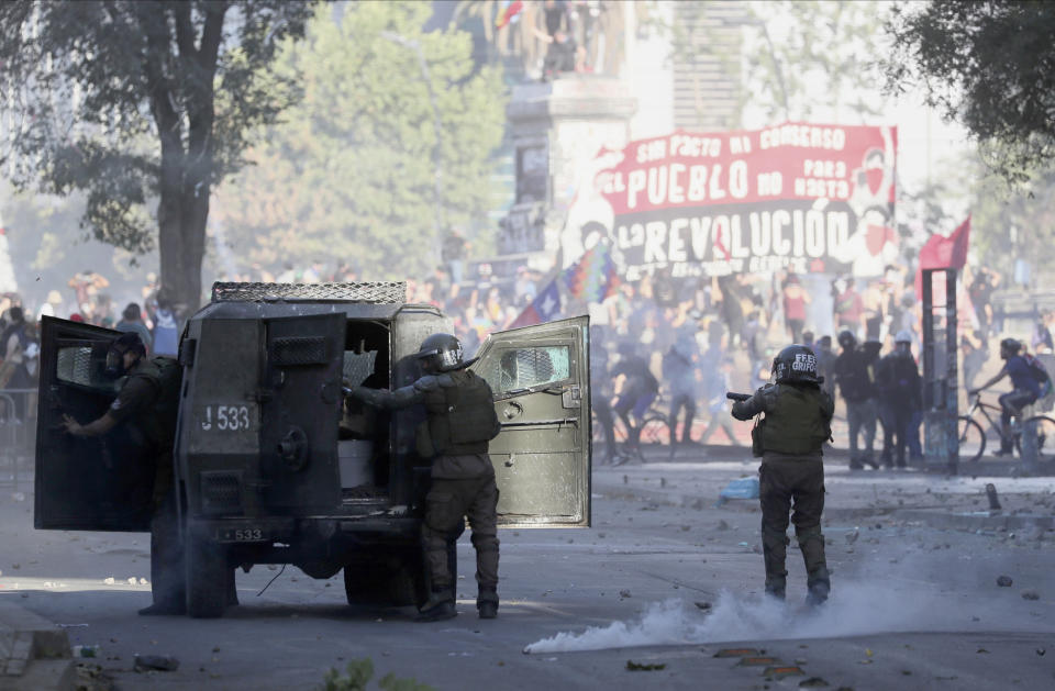 Police clash with anti-government demonstrators in Santiago, Chile, Friday, Dec. 20, 2019. Chile marks a second full month of unprecedented social revolt that has not only altered the country's political landscape but also prompted a referendum on reforming the country's dictatorship-era. (AP Photo/Fernando Llano)