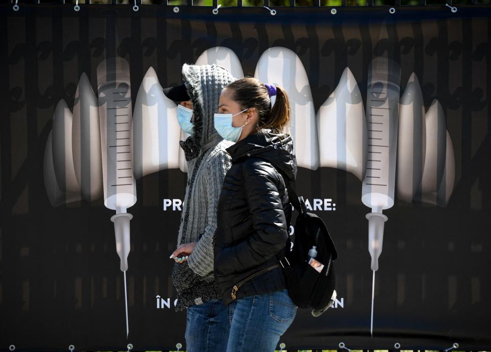<p>Dos jóvenes con mascarilla pasan junto a un cartel que muestra jeringuillas como si fueron colmillos de vampiro. La imagen ha sido tomada en el célebre castillo de Bran, en Rumanía. (Foto: Daniel Mihailescu / AFP / Getty Images).</p> 
