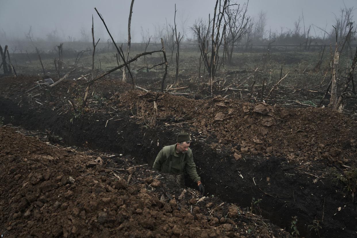 A Ukrainian soldier in a trench surrounded by fog and burnt trees