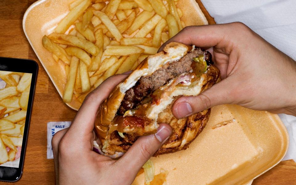 Men eating hamburger and fries - Getty