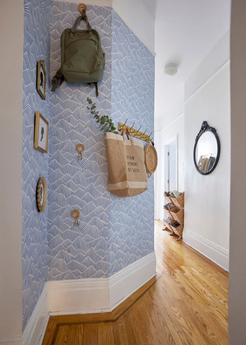Blue wallpaper on hallway wall with hooks and silhouette artwork.