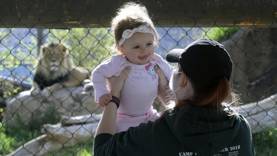 Holly Stuart holds her daughter Savannah during a visit to Utah's Hogle Zoo Saturday, May 2, 2020, in Salt Lake City. The zoo is one of many Utah businesses reopening Saturday amid the Coronavirus pandemic after multi-week closure. The zoo will restrict the number of guests who enter per day to help with social distancing. (AP Photo/Rick Bowmer)