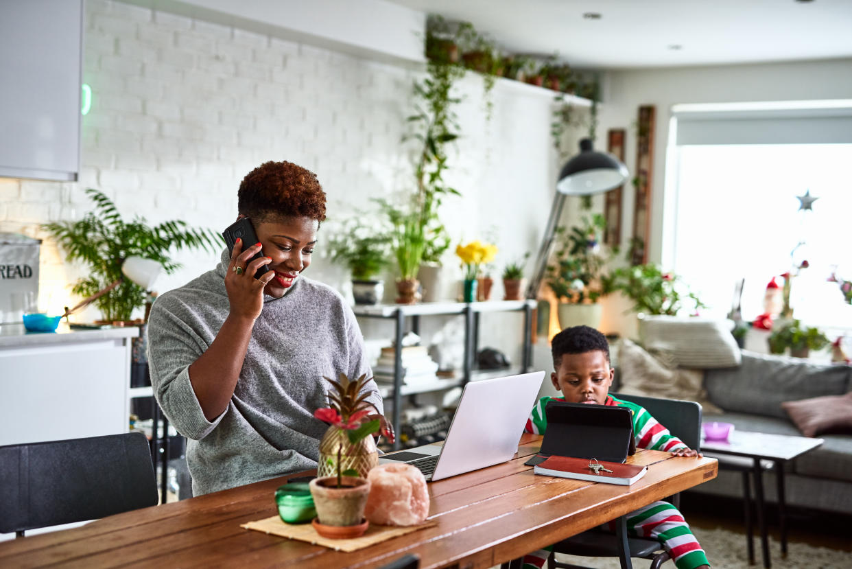 Mid adult woman on phone with laptop at dining table, son using digital tablet, role model, working mother, efficiency