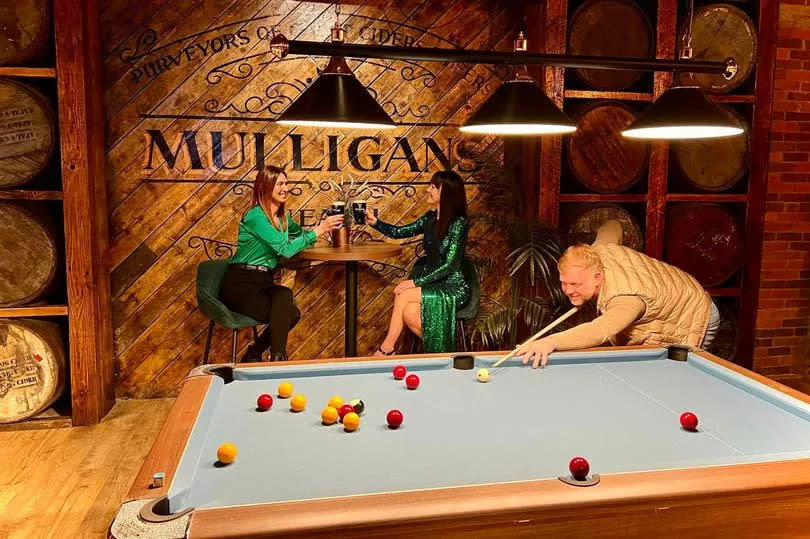 Inside Mulligans in Neath: two ladies 'cheers' their pints of Guiness at a table in the bar, whilst a man plays pool