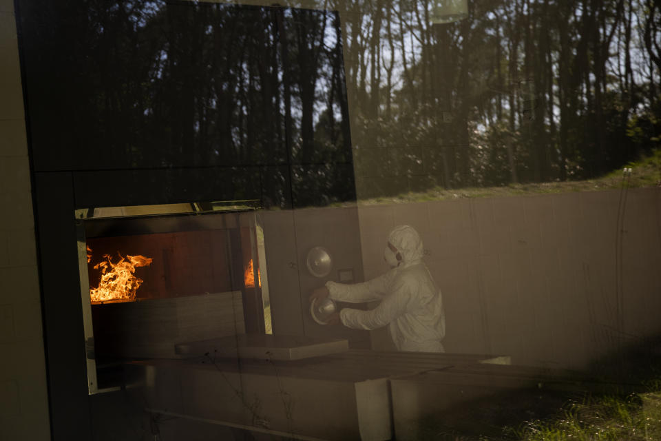 A worker, wearing a full protective gear, moves the casket of someone who has died of Covid-19 into the crematorium oven during a partial lockdown to prevent the spread of coronavirus at the Pontes crematorium center in Lommel, Belgium, Thursday, April 16, 2020. (AP Photo/Francisco Seco)