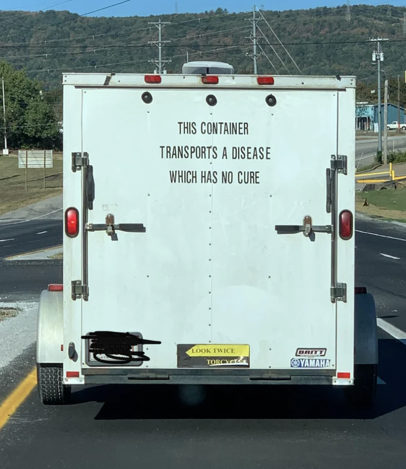 Truck with a sign reading "This container transports a disease which has no cure" and urging to "look twice" for motorcycles