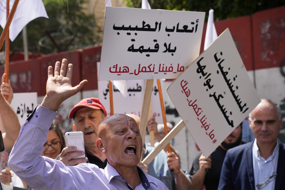 A medical worker shouts slogans as other hold Arabic placards that read: "Doctors fees are worthless, Hospitals will close their doors, we cannot continue like this," as they protests with doctors the deteriorating economic conditions, outside the Central Bank, in Beirut, Lebanon, Thursday, May 26, 2022. The syndicates of doctors in Beirut and the North as well as the Syndicate of Private Hospital Owners declared a two-day general strike Thursday and Friday. (AP Photo/Hussein Malla)