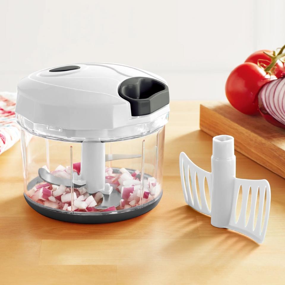 A white food chopper with onions inside with a white plastic piece