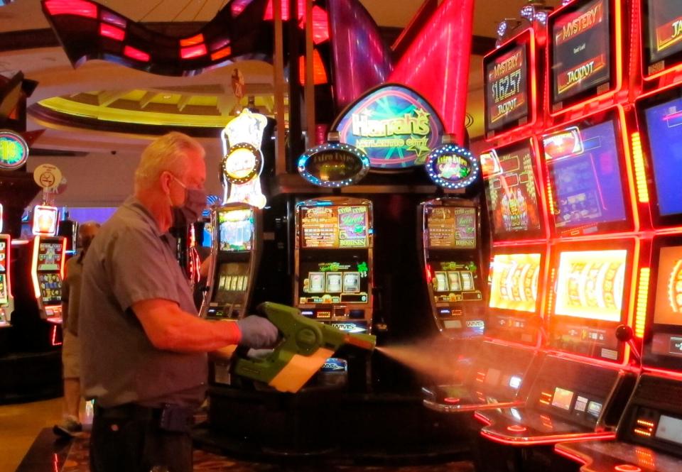 Steven Ford, a worker at Harrah's casino in Atlantic City, N.J., sprays slot machines with disinfectant Wednesday, July 1, 2020, as the casino prepared to reopen after 3 1/2 months of being shut down due to the coronavirus.