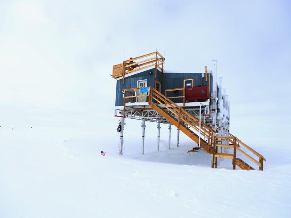 A building on stilts in the snow is surrounded by white snowy conditions on Greenland's summit.