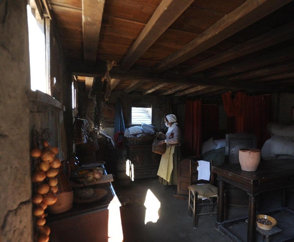 Scenes from the Pilgrim Village at Plimoth Patuxet living museum. An interpreter, wearing a mask due to COVID-19, works in a replica of a Pilgrim house.