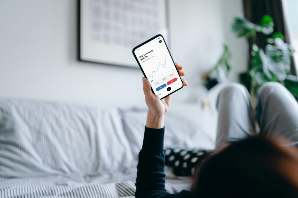 Young Asian woman lying on bed at home, reading financial trading data on smartphone. Financial investment, stock market and exchange, accounting concept