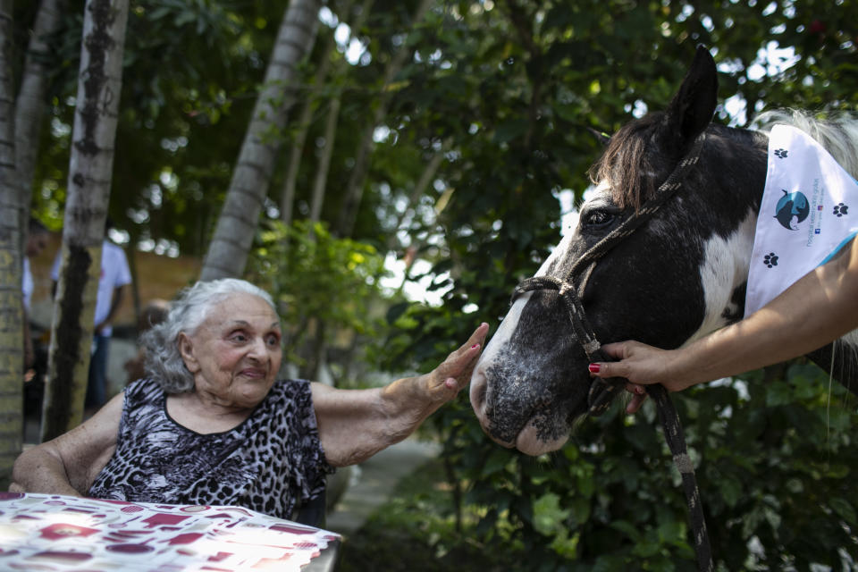 An elderly woman reaches out to pet a horse named Tony at the "Casa de Repouso Laços de Ouro" nursing home in Sepetiba, Brazil, Thursday, Oct. 1, 2020. The Golias organization brought the animals, who they rescued from abandonment, to provide a little relief from the isolation many elderly people feel, cut off from friends and family due to fear of contagion from the new coronavirus. (AP Photo/Bruna Prado)