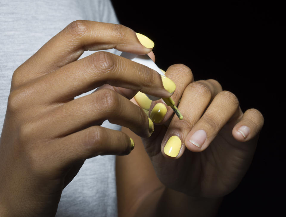 Close-up of young mixed-race woman applying nail varnish, with black background