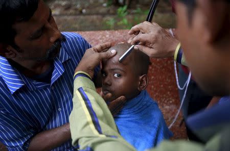 Rajesh, 7, gets his head shaved after cremating his father who died after consuming bootleg liquor at a cremation ground in Mumbai, June 20, 2015. REUTERS/Danish Siddiqui