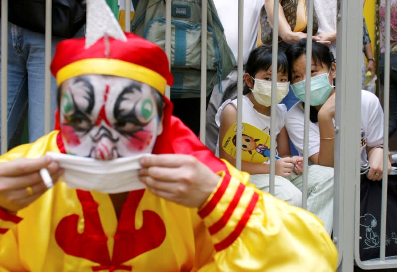 FILE PHOTO: A performer rests in front of onlookers wearing masks to protect themselves from SARS during a parade celebrating Tian Hou, the goddess of the sea, at Hong Kong's rural New Territories