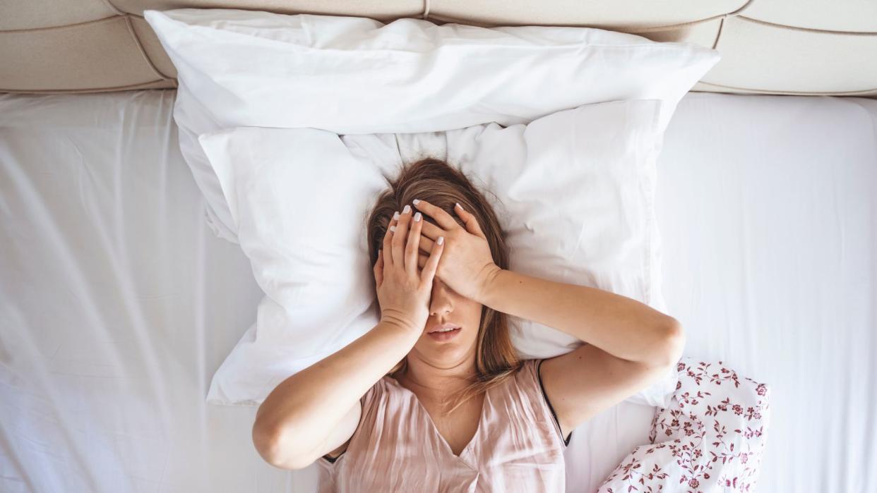  Young woman lies in bed with sleep problems caused by choosing a memory foam hybrid instead of a latex hybrid. 