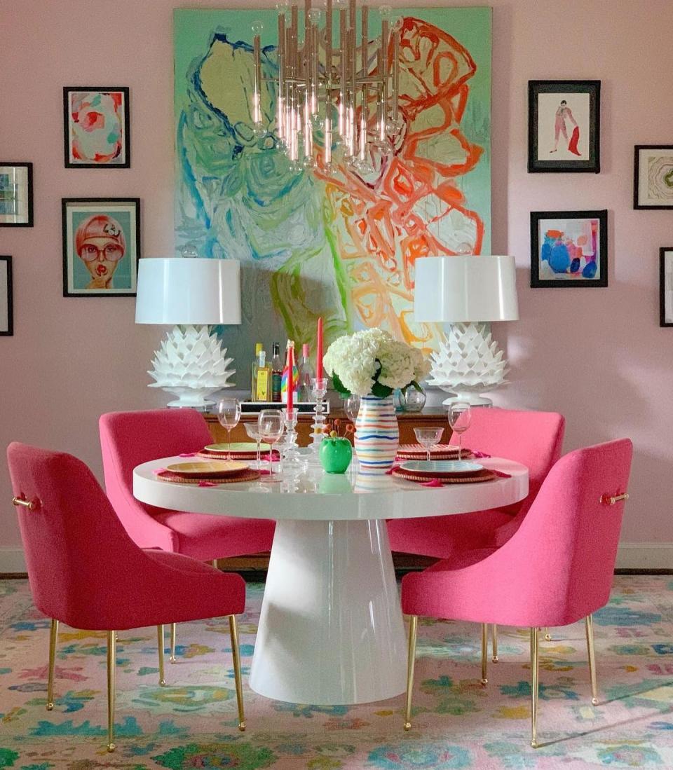 Pink dining room with statement artwork and round table with pink chairs.