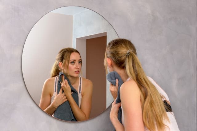 Young Woman Wiping Sweat While Looking In Mirror At Gym