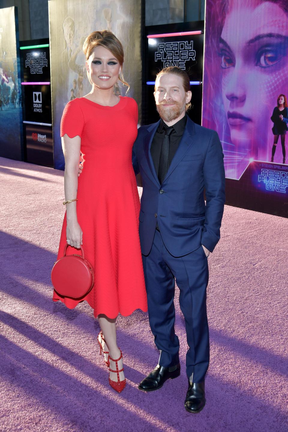 Clare Grant in a red midi-dress and heels standing taller than Seth Green in a blue suit.