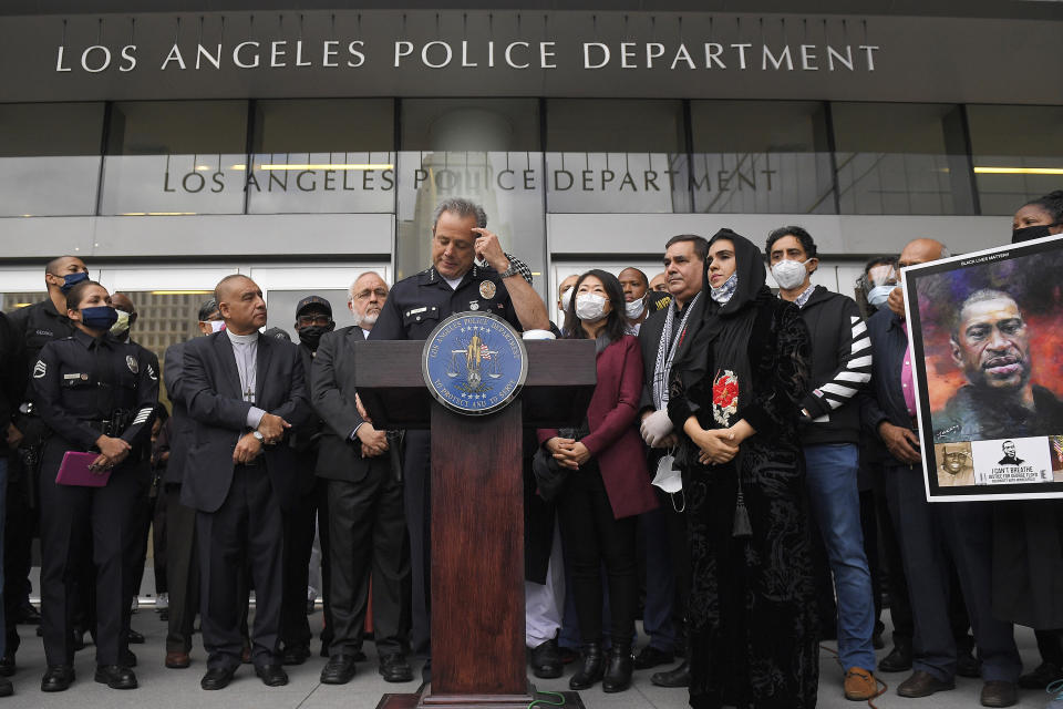 FILE - Los Angeles police chief Michel Moore, left, speaks as someone holds up a portrait of George Floyd during a vigil with members of professional associations and the interfaith community at Los Angeles Police Department headquarters, Friday, June 5, 2020, in Los Angeles. The Los Angeles City Council has voted to slash the Police Department budget by $150 million, reducing the number of officers to a level not seen for more than a decade. The council approved the change Wednesday, July 1, 2020, dropping the number of officers to a little more than 9,700 by next summer. (AP Photo/Mark J. Terrill, File)