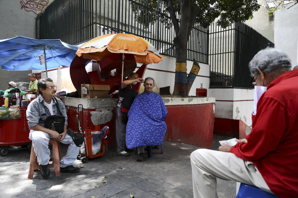 A woman cuts hair on a sidewalk as customers wait for their turn, in downtown Caracas, Venezuela, Wednesday, March 6, 2019. As the political and economic crisis deepens, the U.S., Germany and some 50 other countries consider Venezuela's President Nicolas Maduro's re-election invalid and have urged him to step aside so the country can prepare for elections. Maduro says he is the target of a U.S.-backed coup plot. (AP Photo/Eduardo Verdugo)