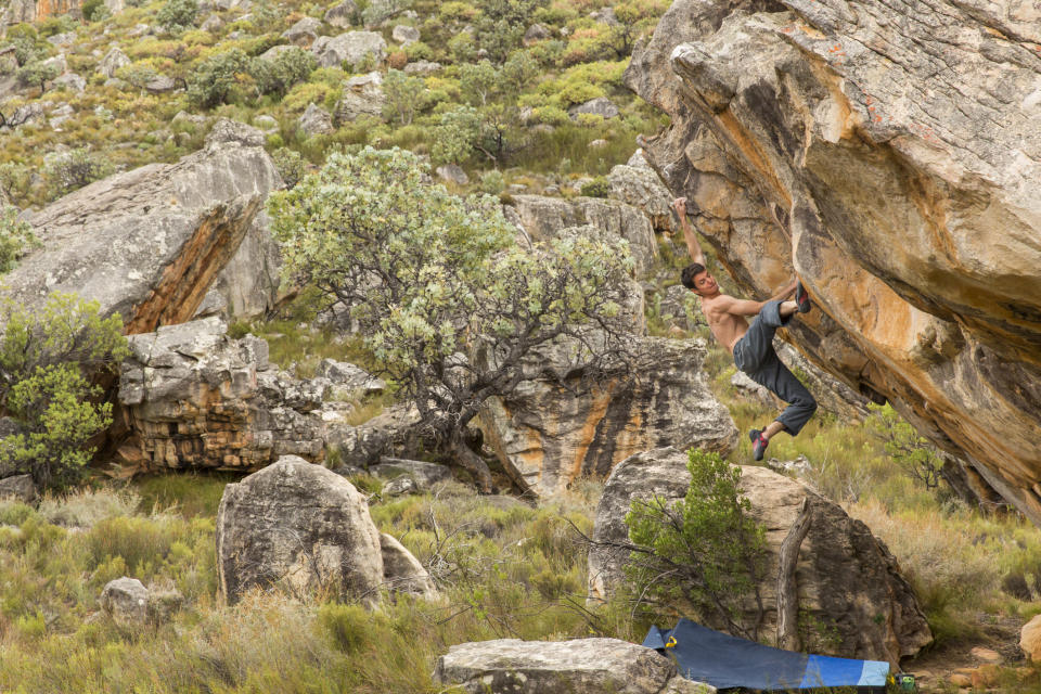 Athletic male climbs outside on a boulder in a grassy, rocky landscape