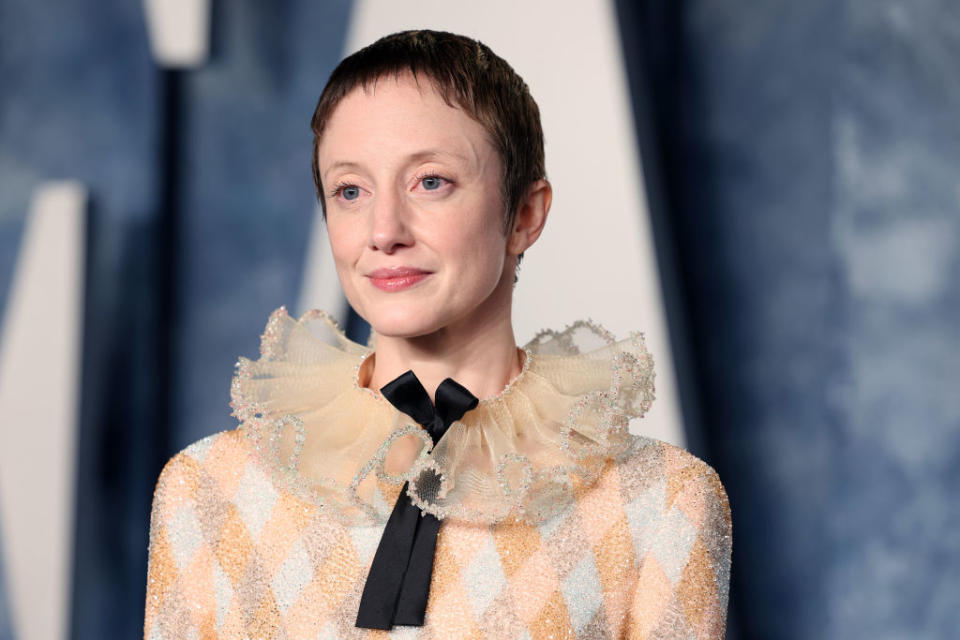 Andrea on a red carpet wearing a patterned outfit with a ruffled collar and bow tie