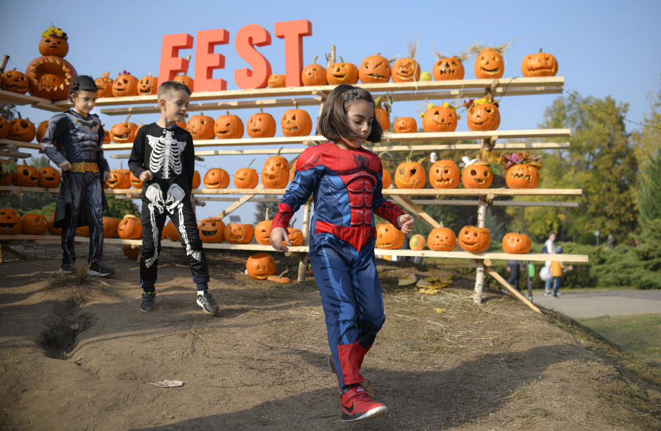 In this Saturday, Oct. 26, 2019 photo children wearing costumes walk by Halloween pumpkins at The Halloween Pumpkin Fest in Bucharest, Romania. (AP Photo/Andreea Alexandru)