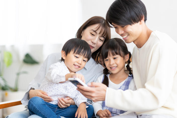 An Asian family of four looking at a smartphone, illustrating a story on minimum income to fulfil basic needs. 