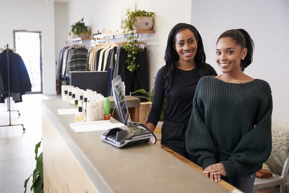 Two women are behind a counter at a clothing store.