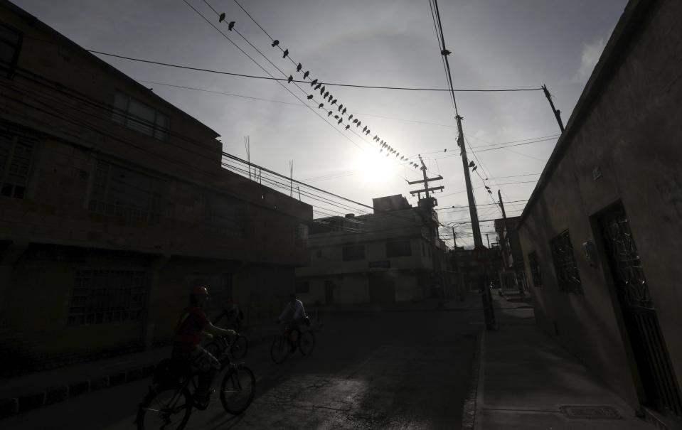 Pigeons perch on electricity cables above two cyclists making their way through a street devoid of cars in Bogota, Colombia, Wednesday, Aug. 5, 2020. While restrictions to curb COVID-19 have been lifted in many places, a nationwide stay-at-home order remains in effect in Colombia more than four months after taking effect. (AP Photo/Fernando Vergara)