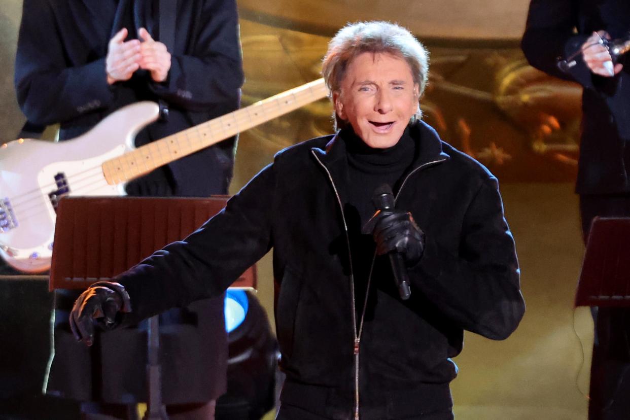 barry manilow holding a micriphone and smiling on stage