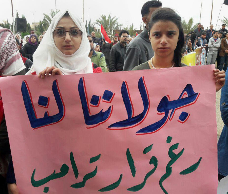 In this photo released by the Syrian official news agency SANA, Syrians hold an Arabic banner that reads, "Golan is ours despite Trump's decision," during a protest against U.S. President Donald Trump's move to recognize Israeli sovereignty over the Israeli occupied Golan Heights, in Deir el-Zour, Syria, Tuesday, March 26, 2019. Syria's state news agency says thousands of Syrians have held gatherings in the streets of different cities to protest Trump's signing of a declaration reversing US policy on the Golan Heights. (SANA via AP)