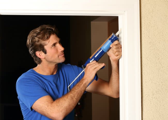 Man uses a caulk gun to caulk around door frame.