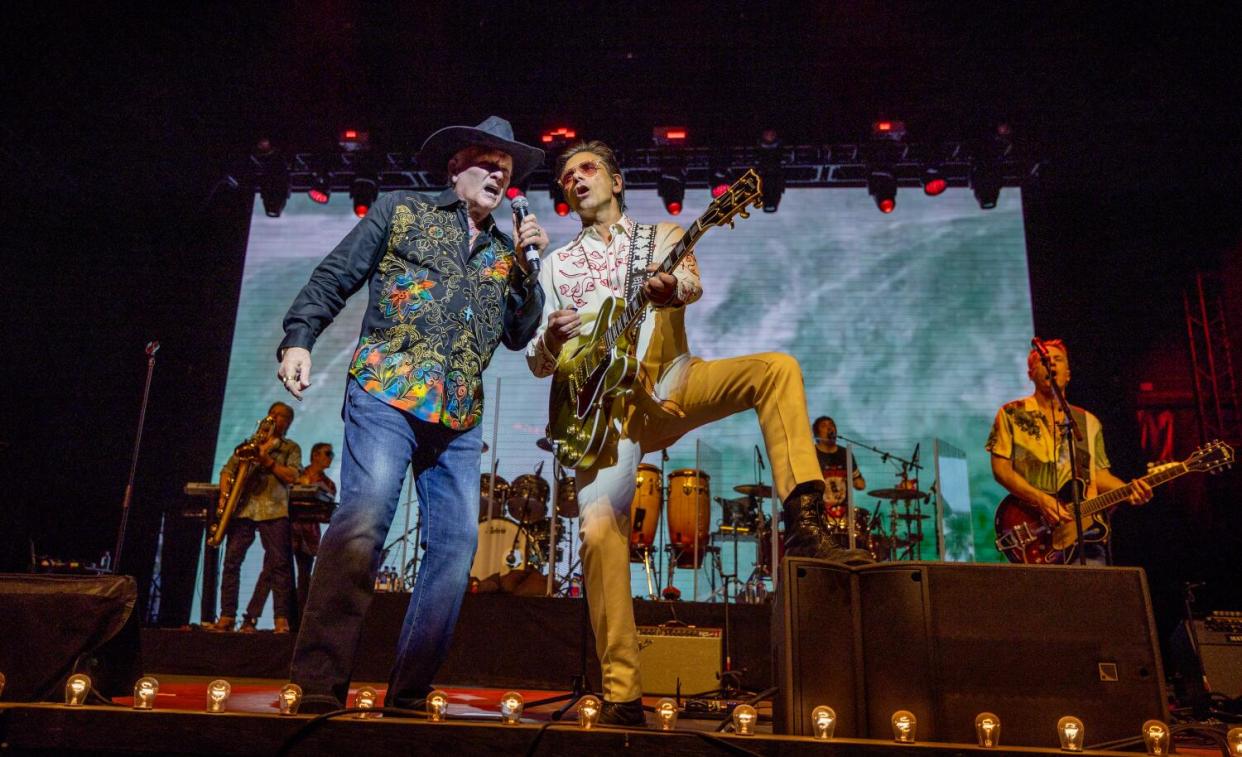 The Beach Boys' Mike Love, left, sings, and John Stamos plays guitar on a stage