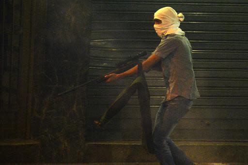 Un joven enmascarado y armado con lo que parece ser un rifle con mirilla telescópica corre por una calle de Caracas, durante los disturbios registrados en la noche del viernes 4 de abril (AFP | Juan Barreto)