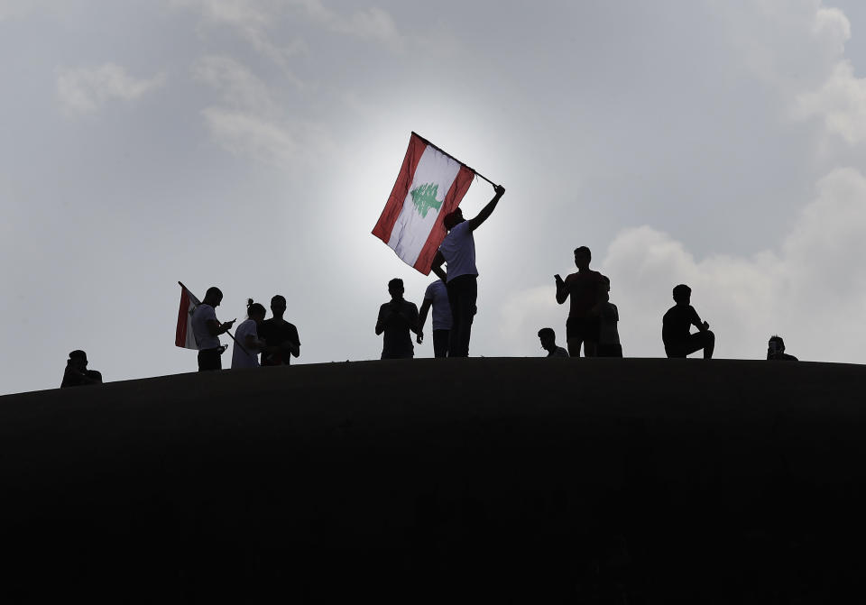 Anti-government protesters wave a Lebanese flag, as they stand on the Dome City Center known as "The Egg," an unfinished cinema leftover from the civil war, as they watch other protesters, in downtown Beirut, Lebanon, Sunday, Oct. 20, 2019. Tens of thousands of Lebanese protesters of all ages gathered Sunday in major cities and towns nationwide, with each hour bringing hundreds more people to the streets for the largest anti-government protests yet in four days of demonstrations. (AP Photo/Hussein Malla)