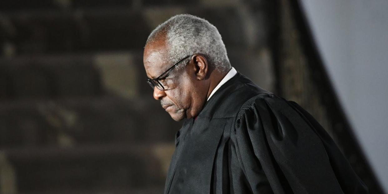 supreme court justice clarence thomas, seen in profile, is standing while wearing his black justice robes and black glasses, he is looking down with a neutral expression on his face