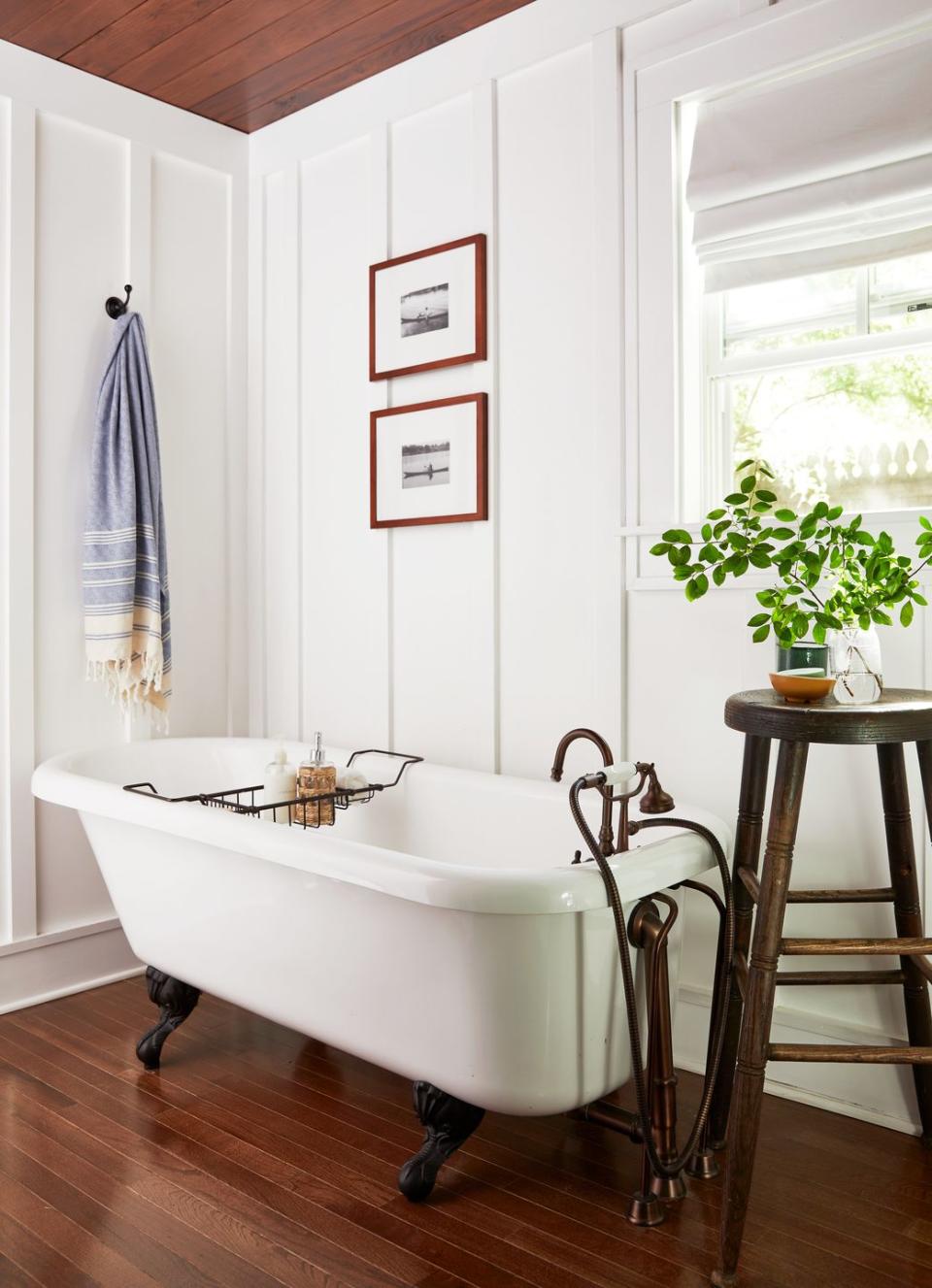 claw foot tub on wood floors with antique postmaster's stool next to it