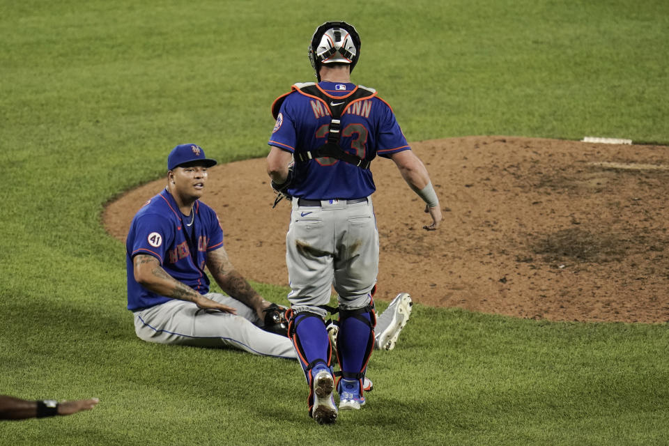 New York Mets starting pitcher Taijuan Walker, bottom, sits in front of the pitching mound after he stopped a sharp line drive by Baltimore Orioles' DJ Stewart and threw hime out at first base during the eighth inning of a baseball game, Wednesday, June 9, 2021, in Baltimore. Mets' catcher James McCann approaches him to check on him. Walker stayed in the game. (AP Photo/Julio Cortez)