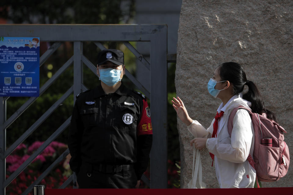 A student wearing a protective face mask to help curb the spread of the new coronavirus waves to teachers as she arrives for the reopening of a primary school in Beijing, Monday, June 1, 2020. With declining virus case numbers, students have gradually returning to their classes in the capital city. (AP Photo/Andy Wong)