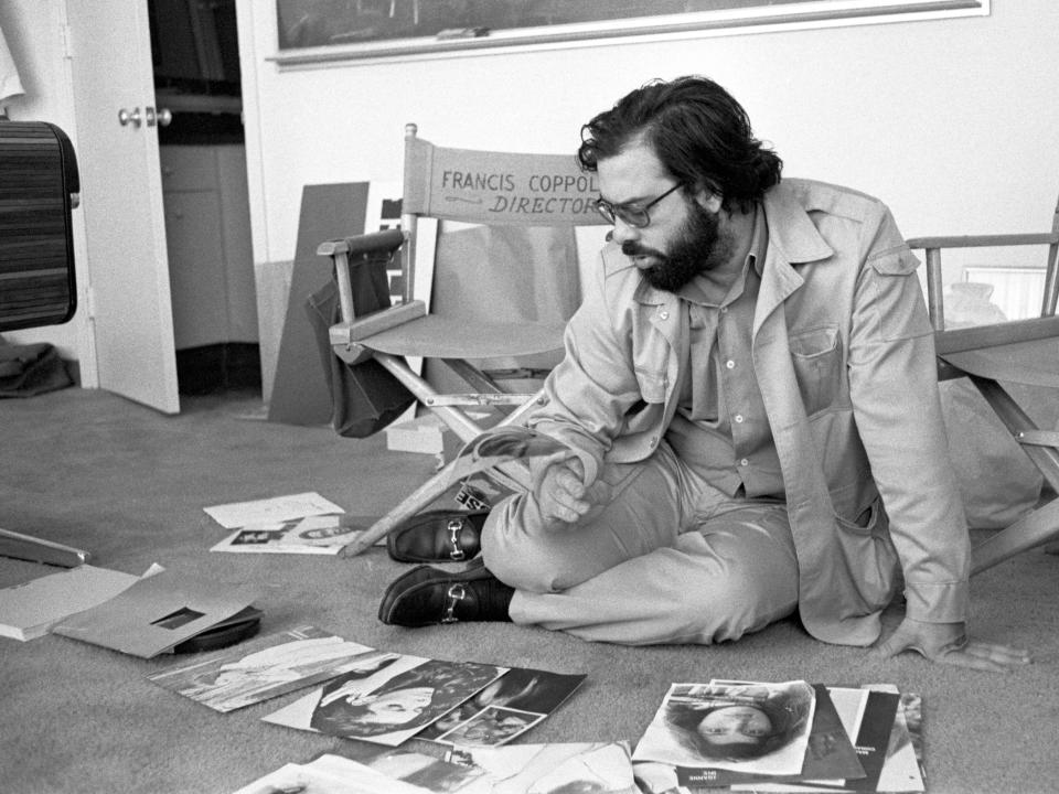 Black and white photo of Coppola sitting on the floor of an office and looking at headshots.