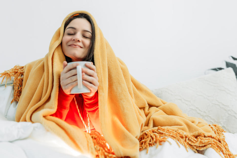 Young woman having coffee under warm bedding