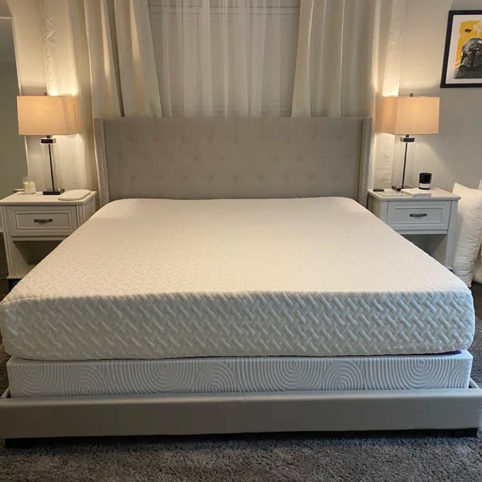 Reviewer's photo of the mattress placed on an upholstered bedframe with a gray tufted headboard