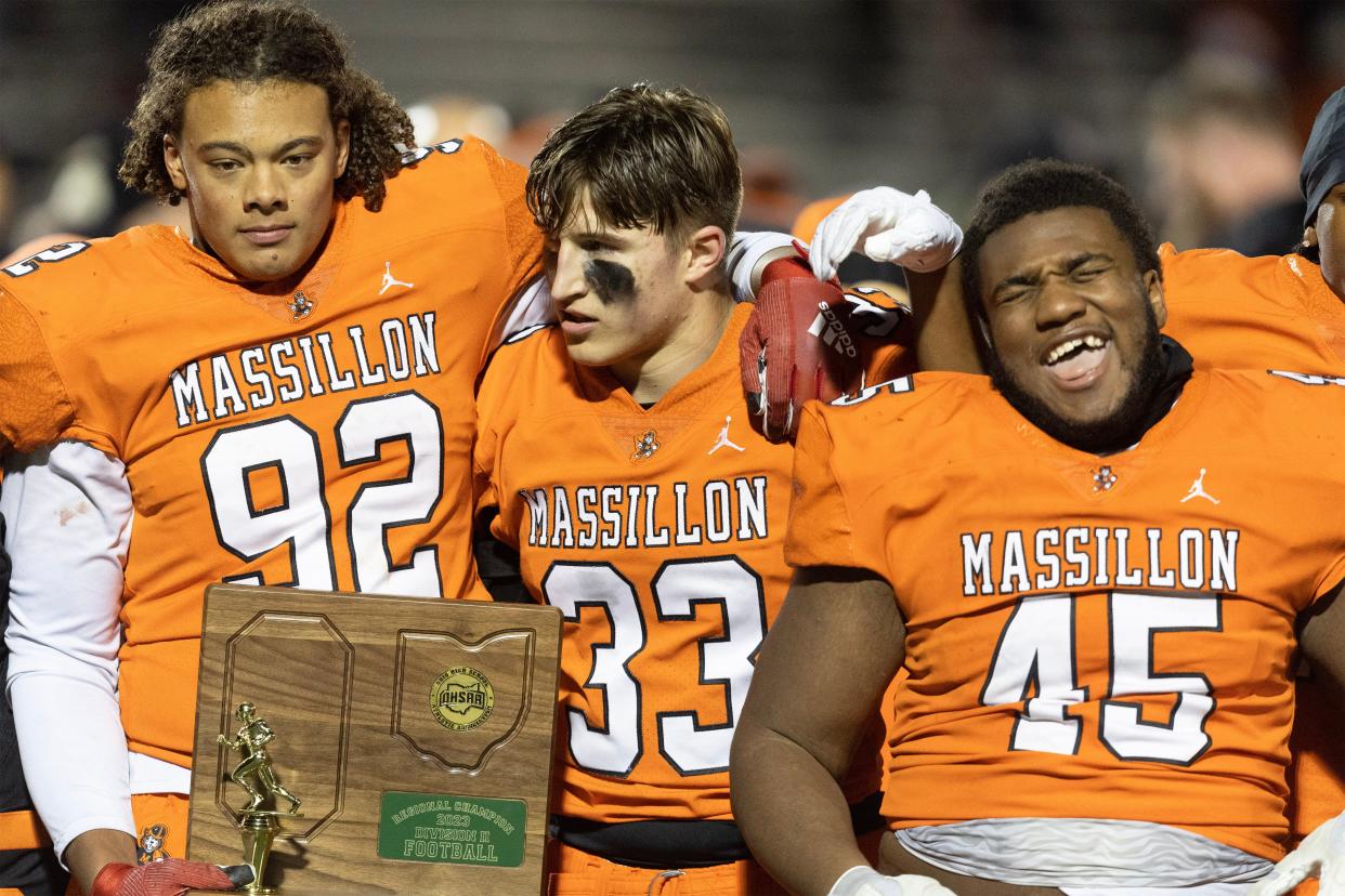 Massillon's Chase Bond (92), Cody Fair (33) and Michael Wright Jr. (45) celebrate with the regional championship trophy after beating Green 31-6, Friday, Nov. 17, 2023, in North Canton.