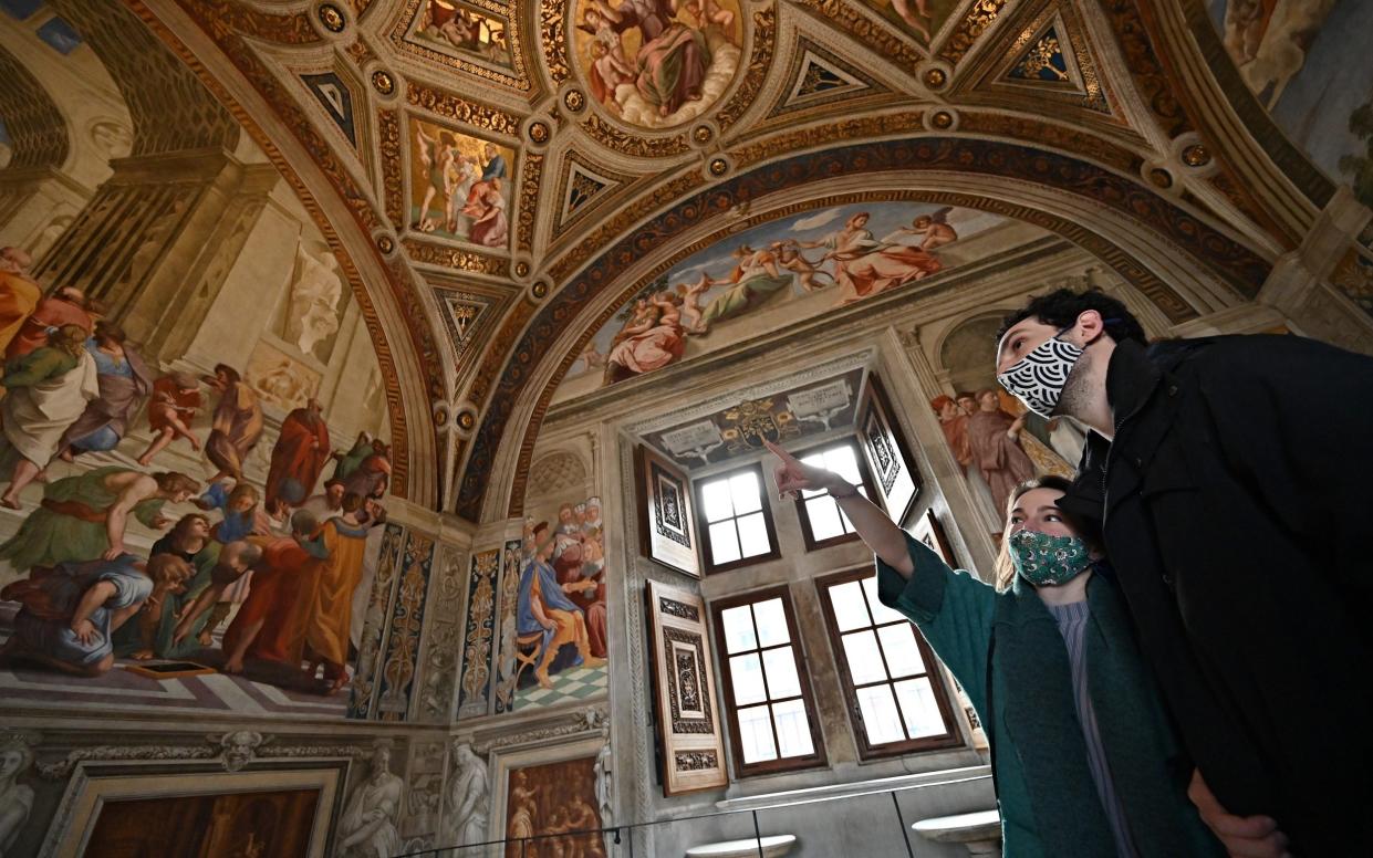 Two people point in interest at frescos, under an ornate ceiling and wearing facemasks